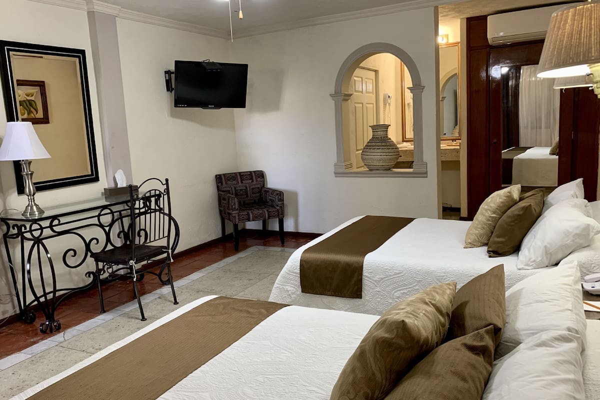 Una habitación de hotel con dos camas, un televisor, una silla y un florero decorativo.