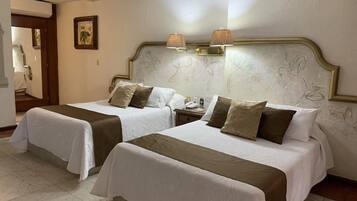 A hotel room with two beds, each with white linens and brown headboards. There are wall-mounted lamps above the beds and a painting on the wall.