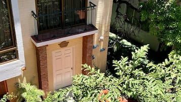 Un edificio residencial con balcón, una puerta y un pequeño jardín con diversas plantas.