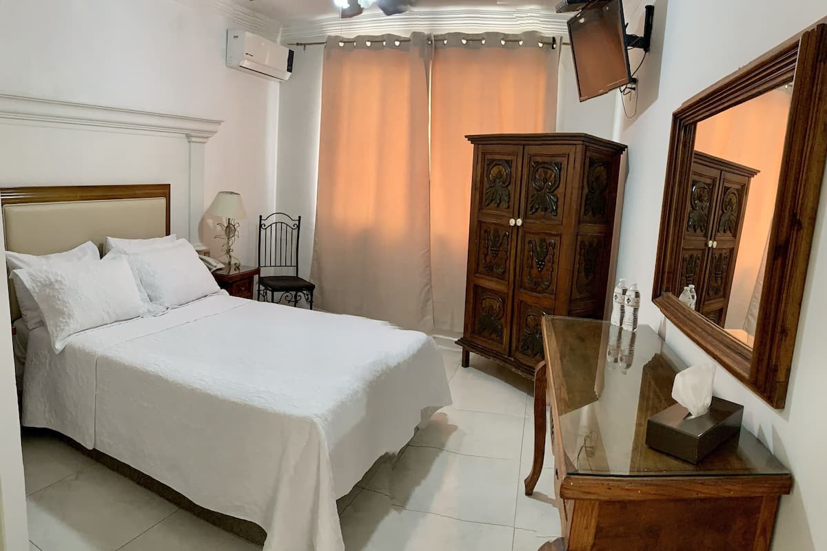 Un dormitorio ordenado con una cama, un armario de madera, una mesita y un espejo.