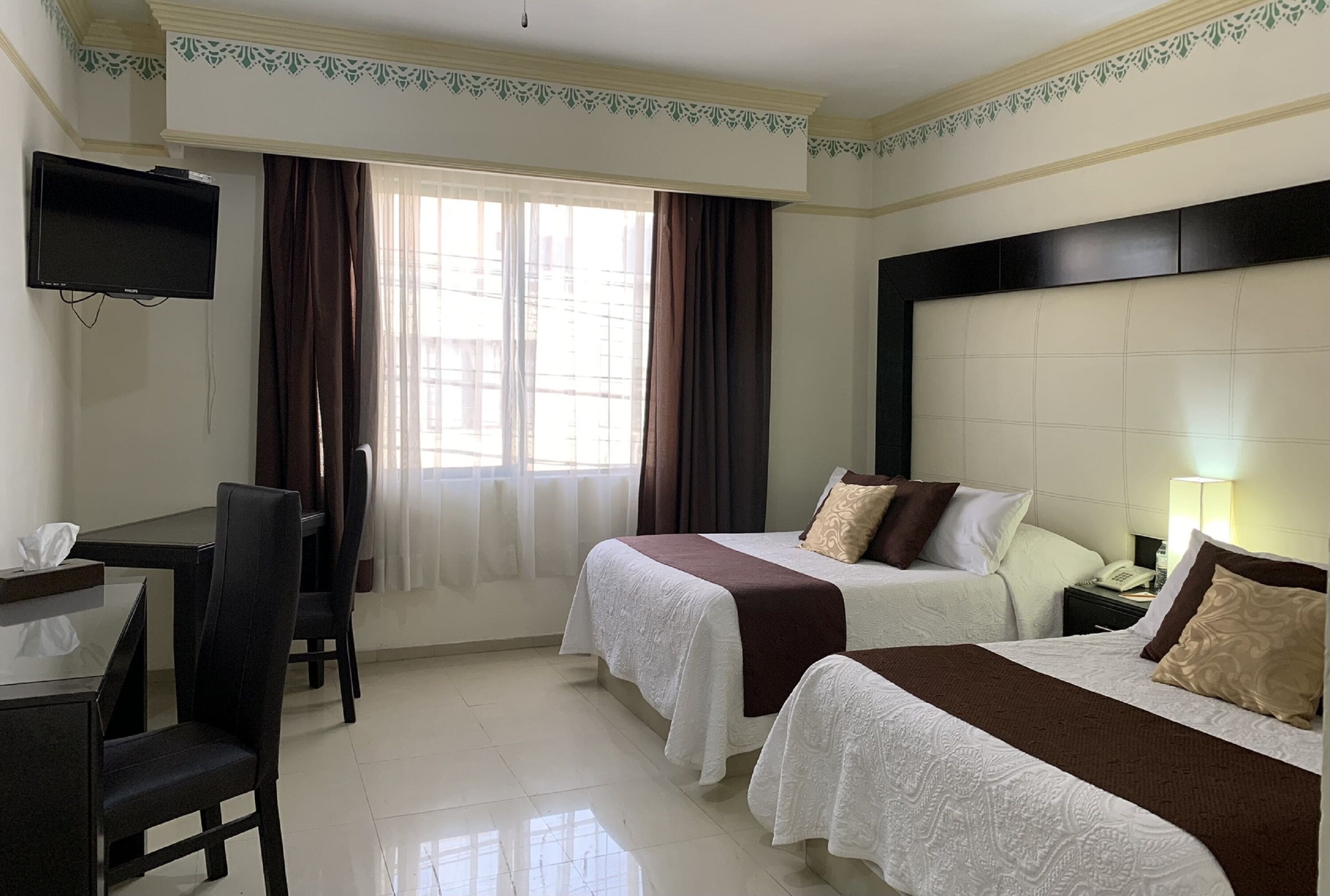 A hotel room with two beds, a desk, a chair, a TV, and a window with curtains.
