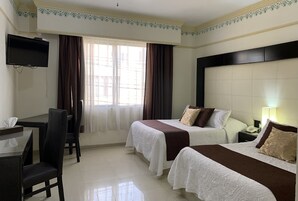 Habitación de hotel con dos camas, un escritorio, una silla, un televisor y una ventana con cortinas.
