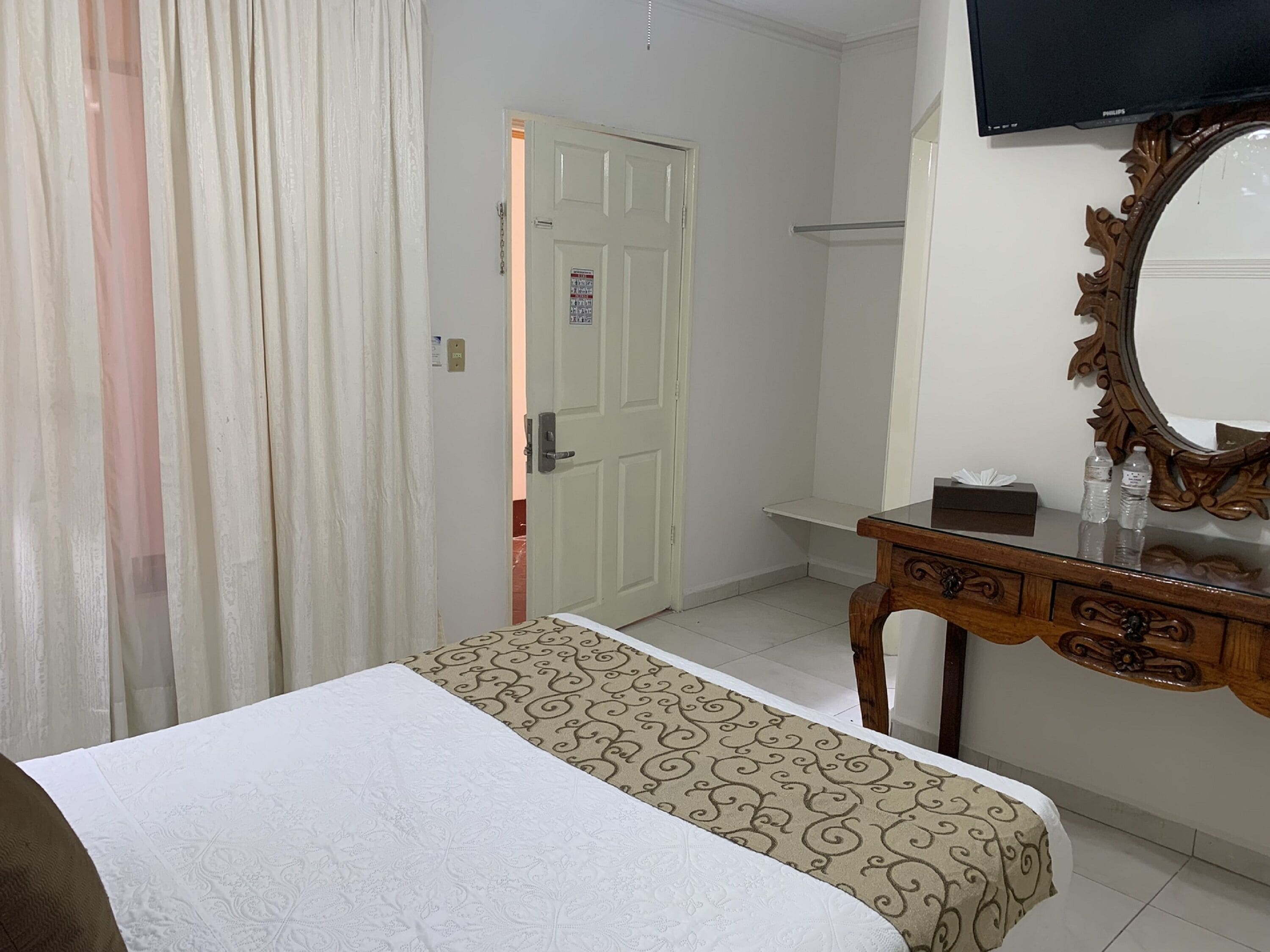 A hotel room with a bed, a wooden dresser, a mirror, and a television.