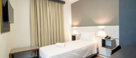 A hotel room with a bed, bedside table, lamp, and a TV mounted on the wall.