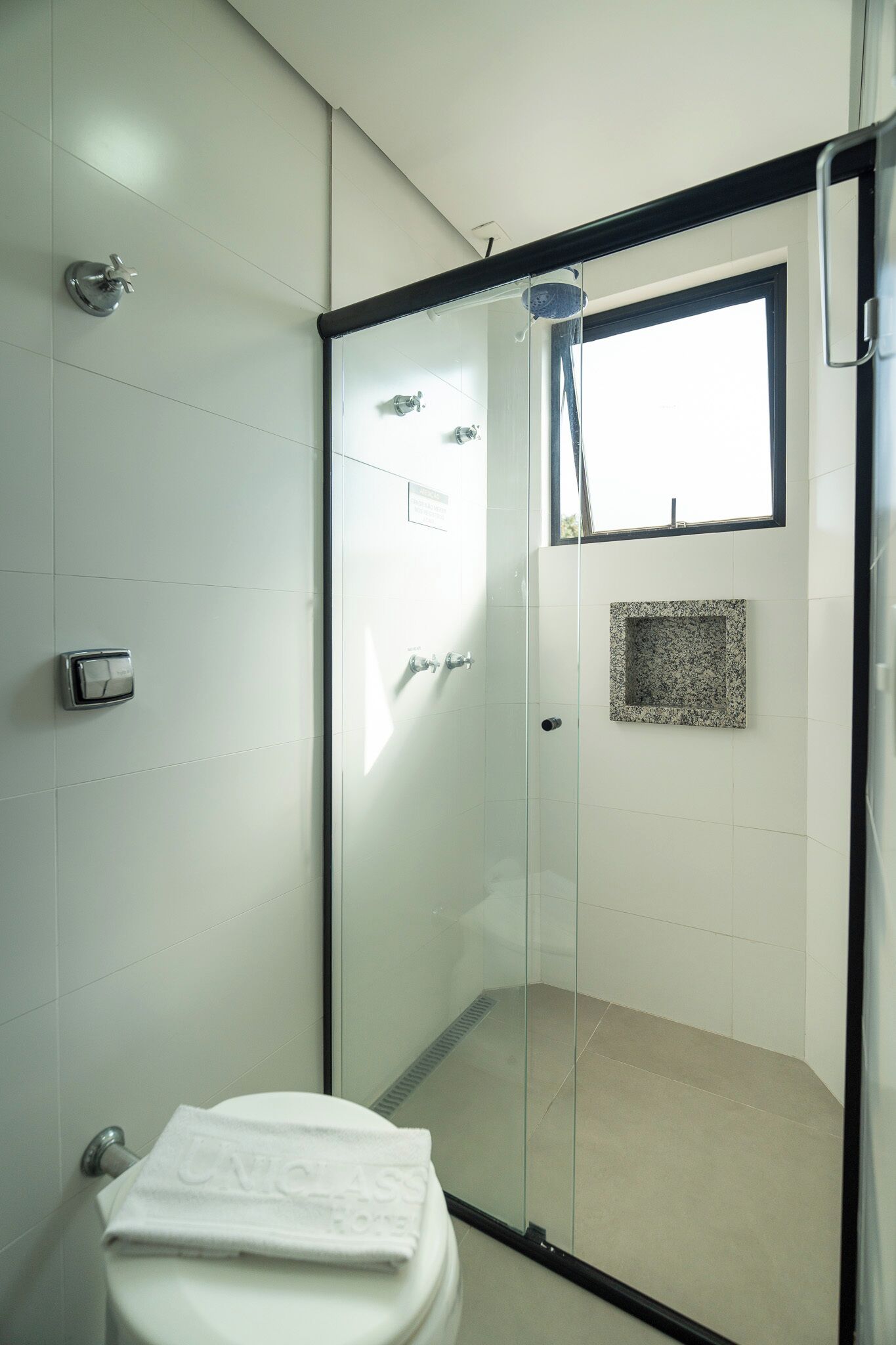 Une salle de bain moderne avec une douche à l’italienne, des toilettes agrémentées d’une serviette blanche et une petite mosaïque décorative sur le mur.