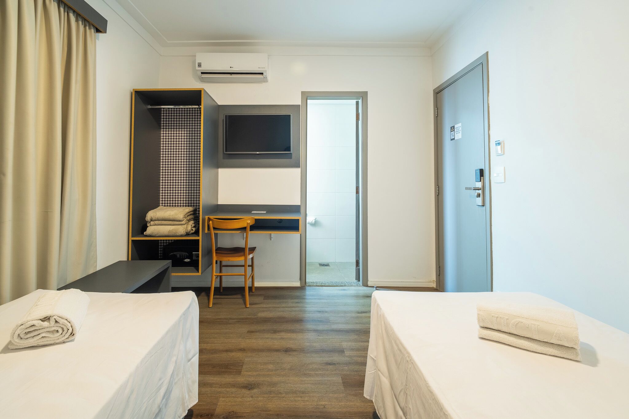 Ein Hotelzimmer mit zwei Betten, einem Schreibtisch mit Stuhl, einem Fernseher und einem Kleiderschrank.