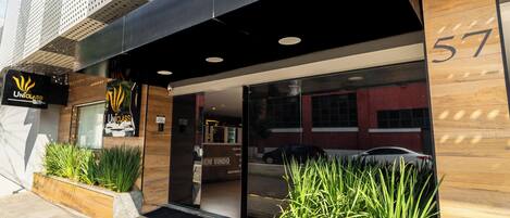 A modern hotel entrance with a black awning, a wooden facade, and a number '57' sign.