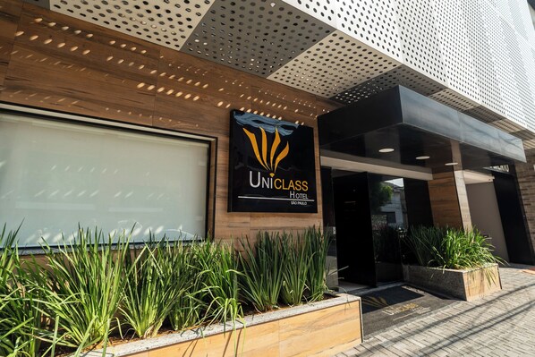 Exterior del Hotel Uniclass en São Paulo, con un diseño moderno que incluye un gran logotipo, entrada de vidrio y jardines bien cuidados.