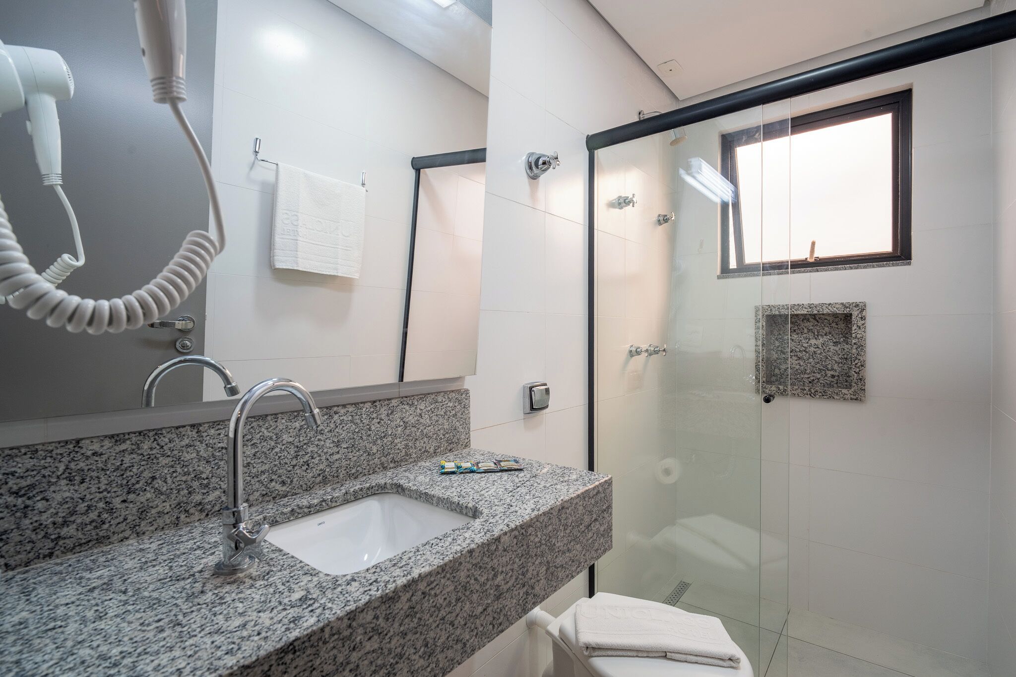 A modern bathroom with a granite countertop, a sink, a hairdryer, a glass shower enclosure, and a small granite accent wall.