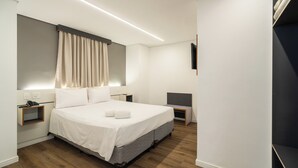 A modern hotel room with a large bed, bedside tables, a flat-screen TV, and a built-in bench. - Uniclass Hotel Lapa (São Paulo)