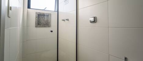 A bathroom with white tiles, a glass shower enclosure, a towel rack, and a window.