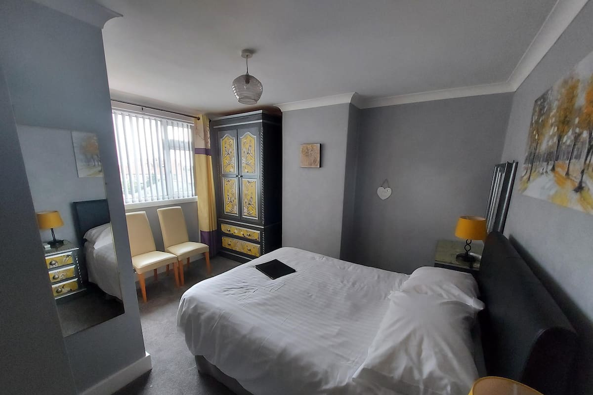 A hotel room with a bed, a desk, a chair, a wardrobe, and a window with blinds.