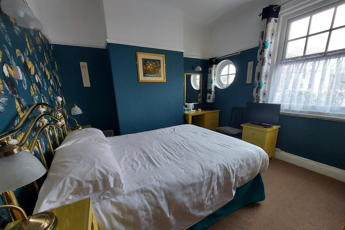 A hotel room with a bed, a desk, a chair, a TV, and a window with curtains.