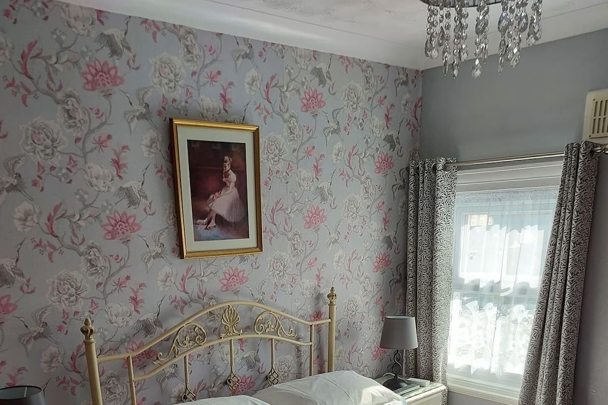 A bedroom with a bed, nightstand, lamp, and a framed picture on the wall.
