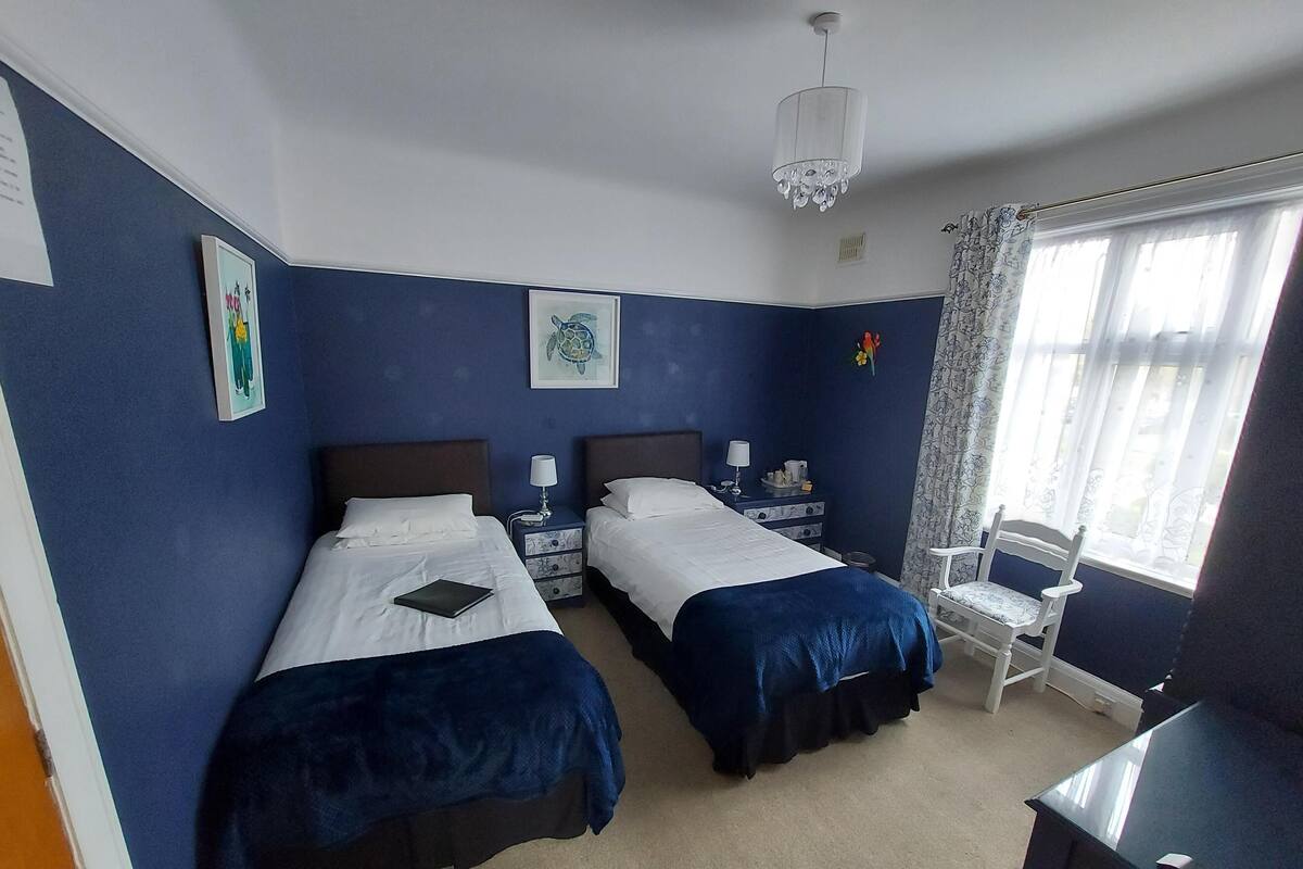A hotel room with two beds, a desk, a chair, a window with curtains, and artwork on the walls.