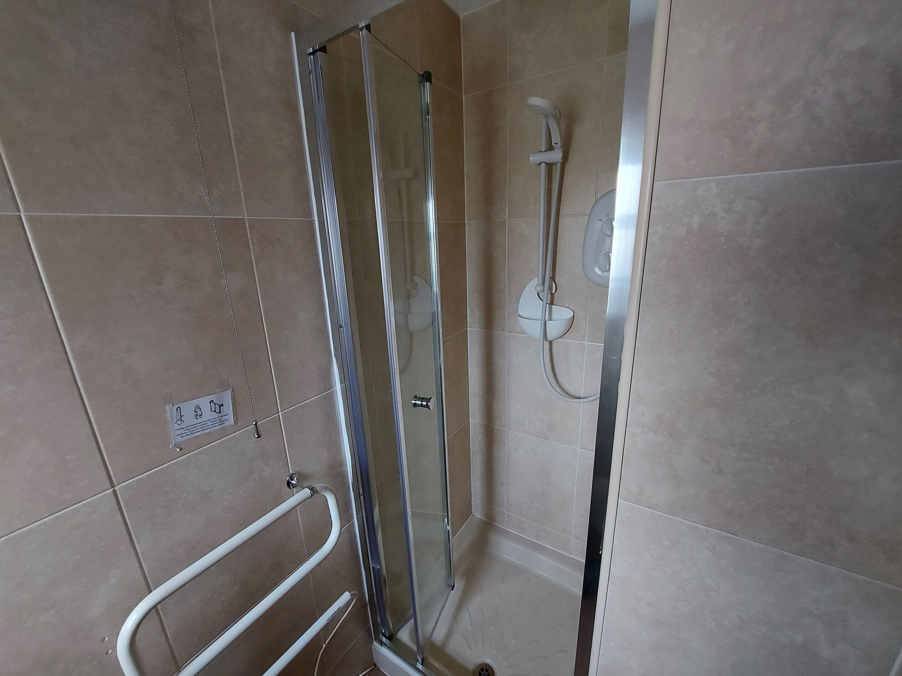 A glass-enclosed shower stall with a handheld showerhead and a wall-mounted faucet.