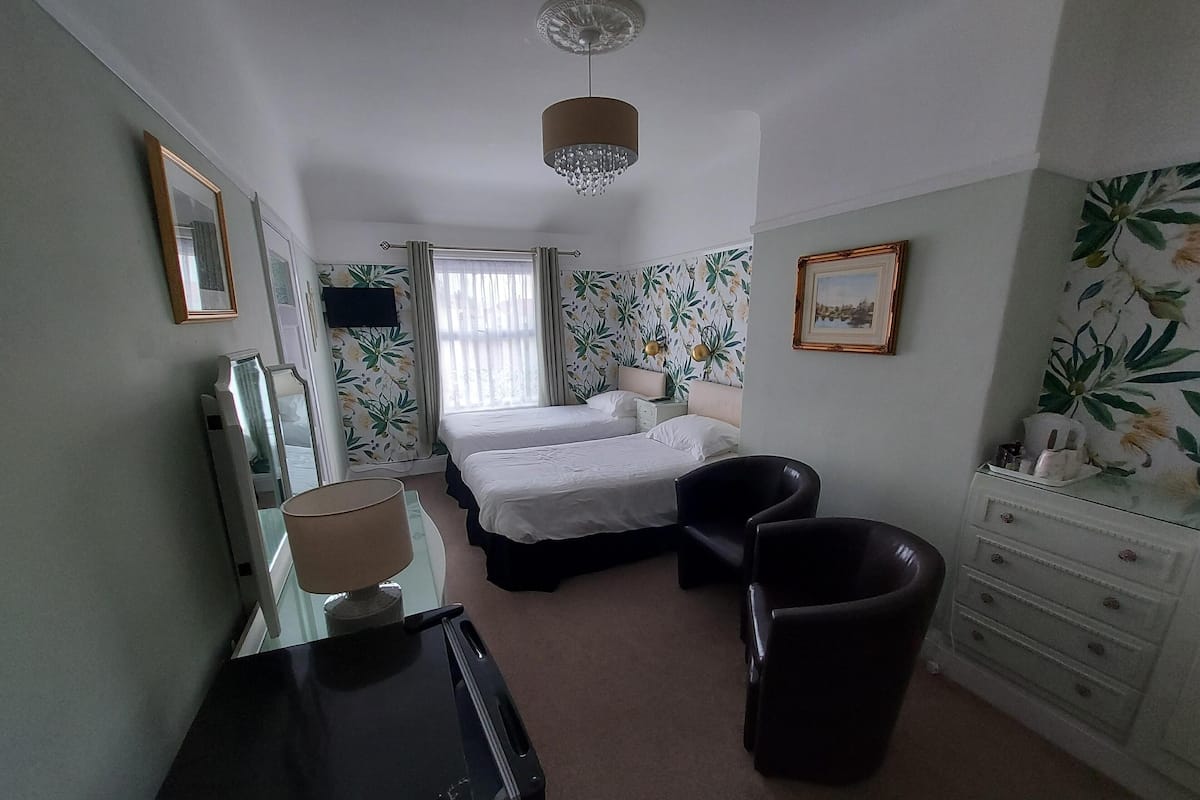 A hotel room with two beds, a desk, a chair, a dresser, and a chandelier.