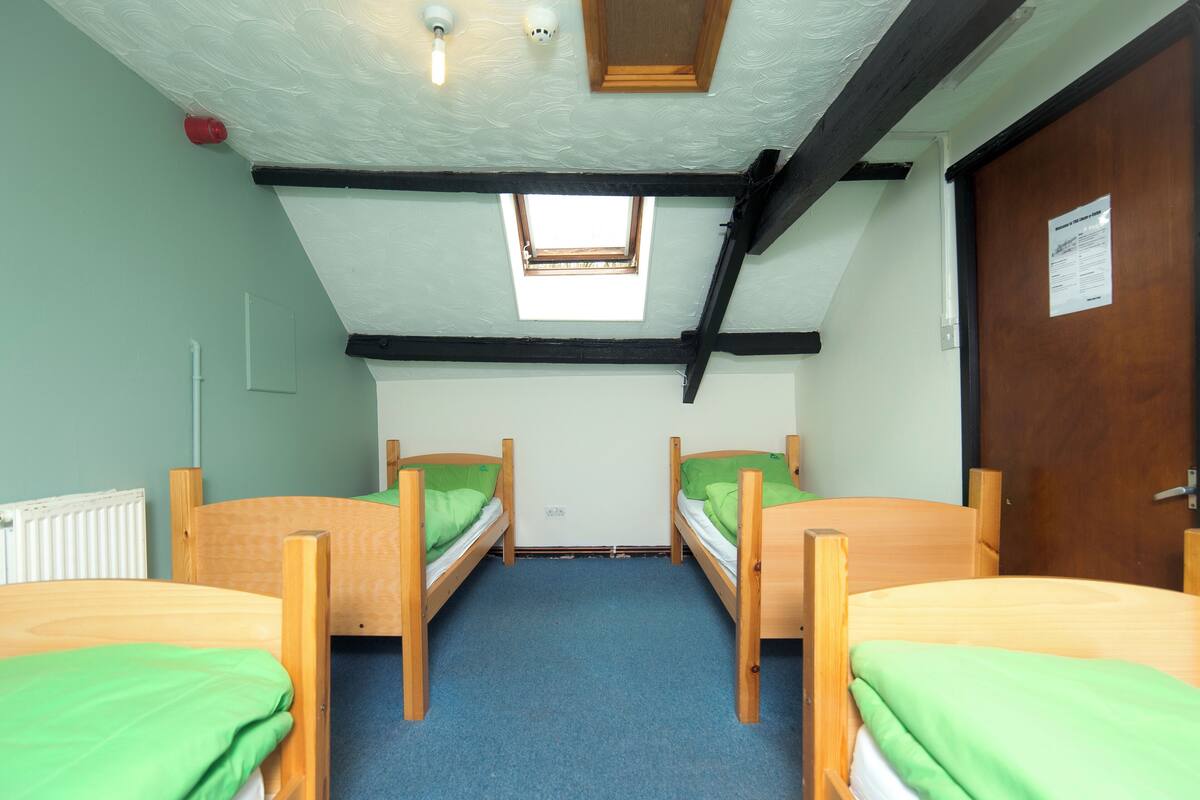 A dormitory room with two wooden bunk beds, a skylight, a radiator, and a door with a sign.