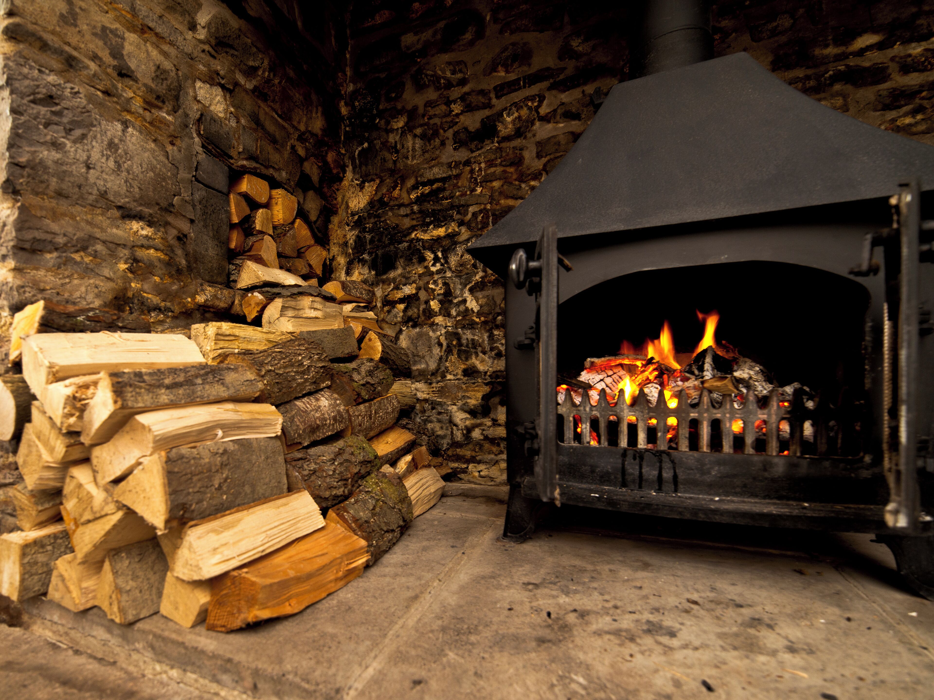 A stone fireplace with a black mantel, wood logs stacked beside it, and a fire burning inside.