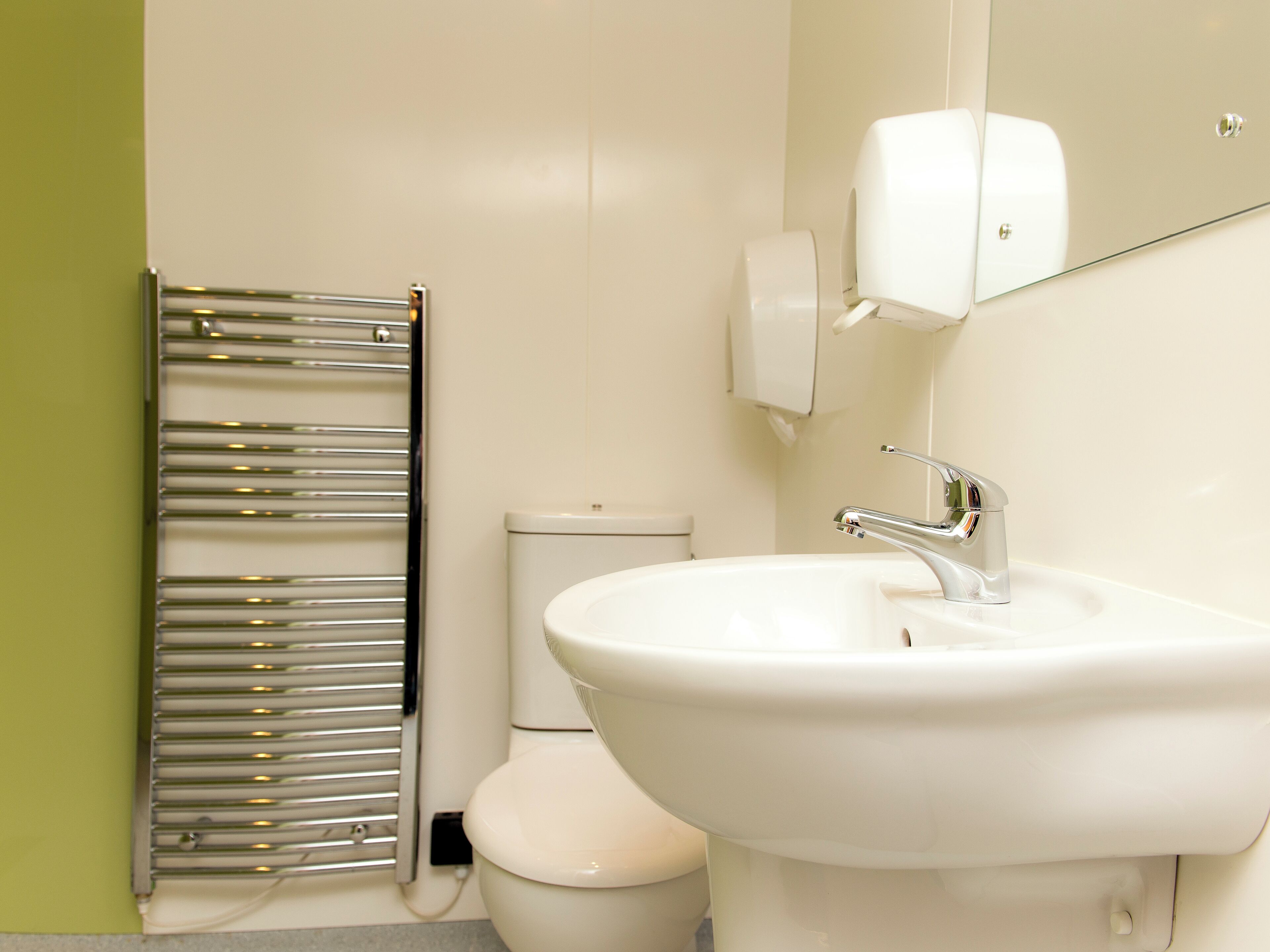 A bathroom with a white sink, a chrome towel rack, a toilet, and a hand dryer.