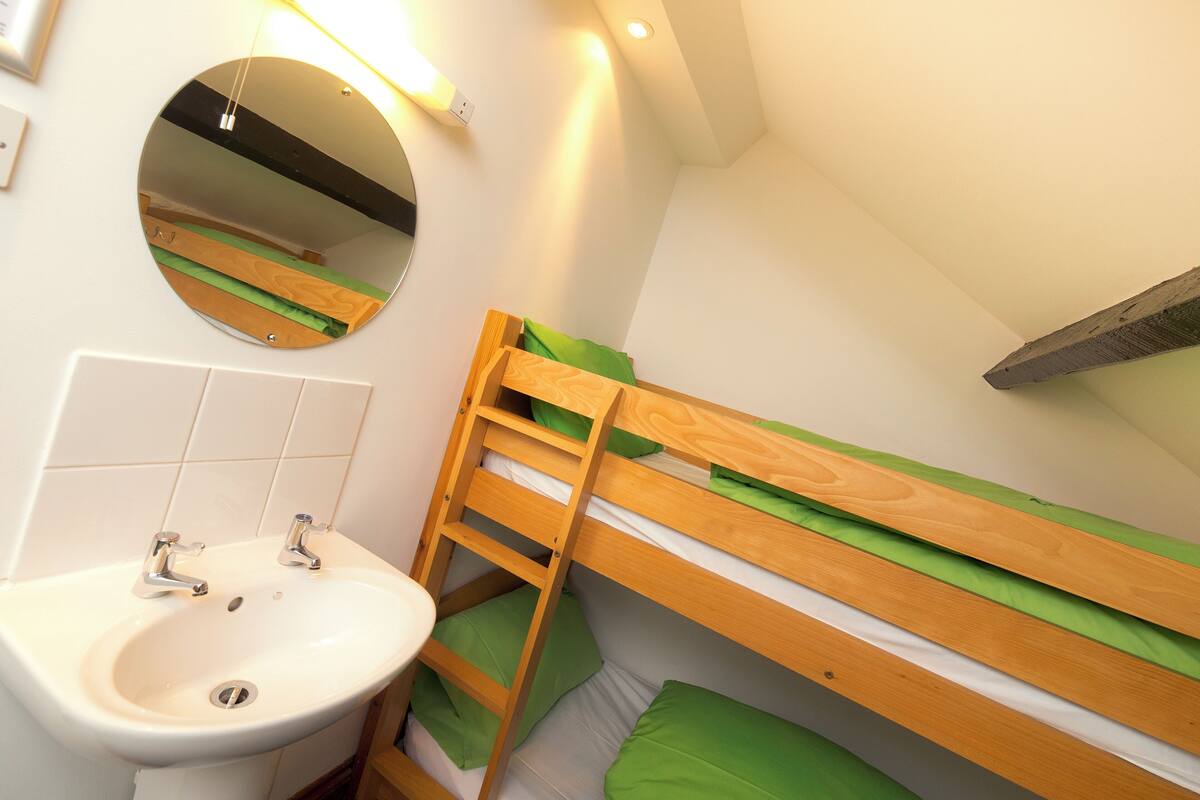 A small, well-lit room with a bunk bed, a round mirror, and a sink.