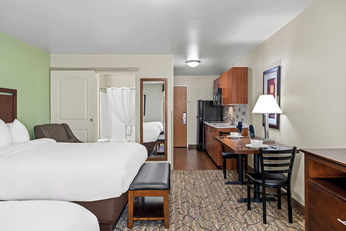Une chambre d’hôtel comprenant un lit, un bureau, une chaise, une salle de bain avec douche et une kitchenette.