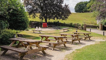 Un área de picnic con varias mesas y bancos de madera, rodeada de abundante vegetación y un gran árbol.