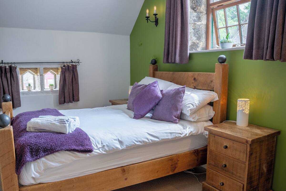 A bedroom with a wooden bed, a nightstand, a dresser, and a window with curtains.