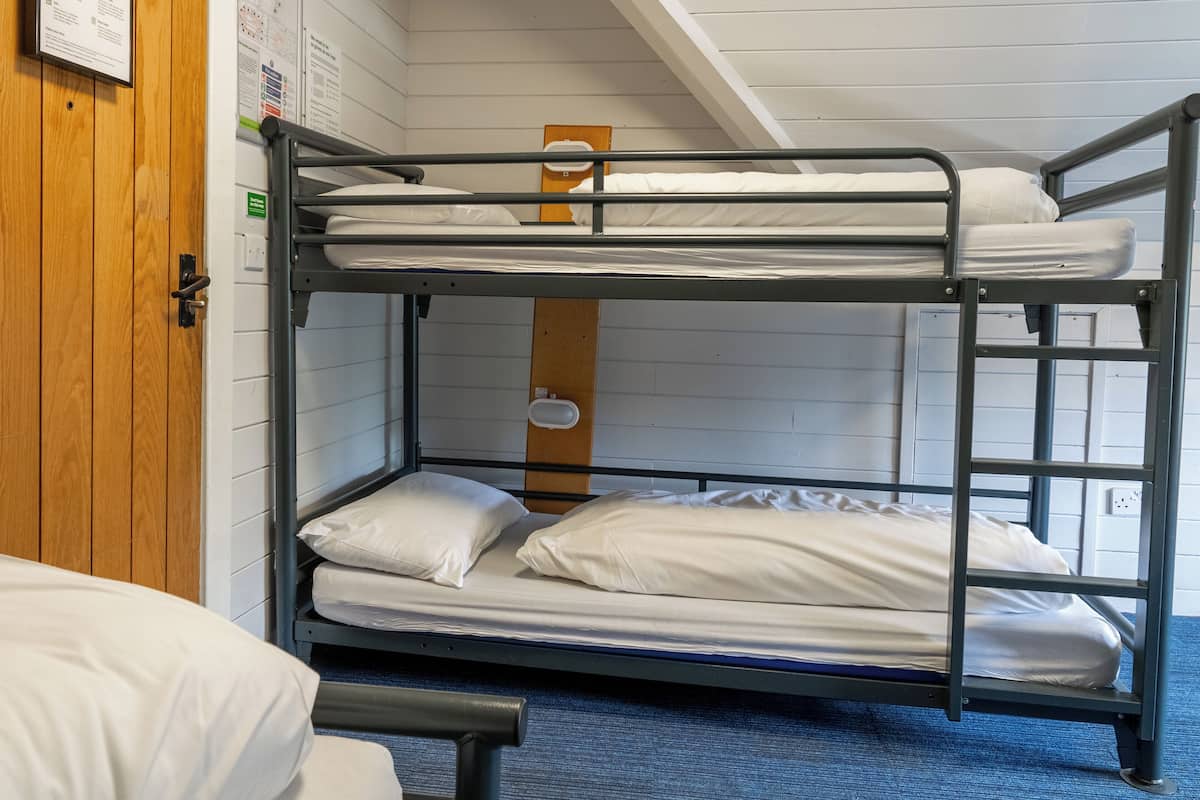 A bunk bed room with a wooden door, a white wall with a bulletin board, and a blue carpet.