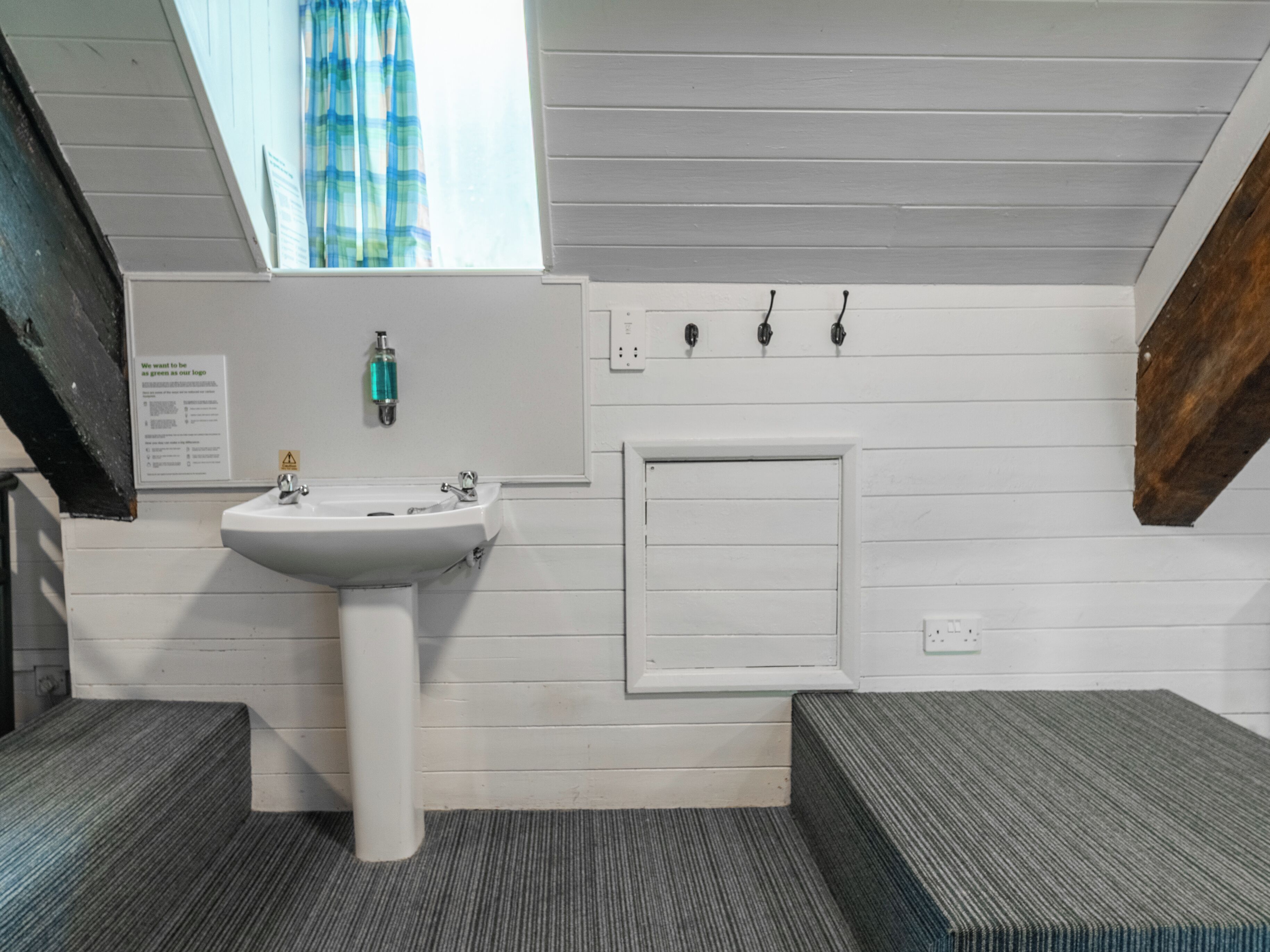 A bathroom with a white sink, a window with a blue curtain, and a wooden bench.
