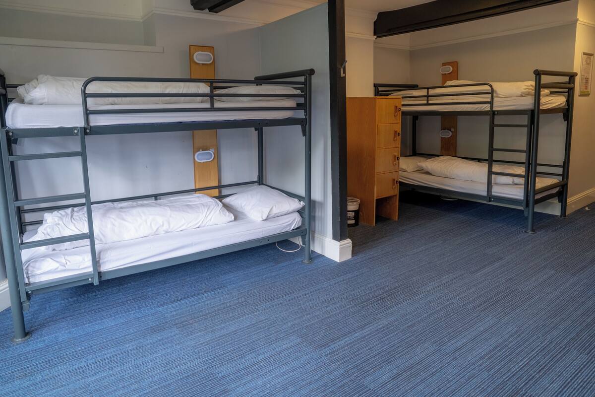 A bunk bed room with a blue carpet, wooden wardrobe, and a white wall.