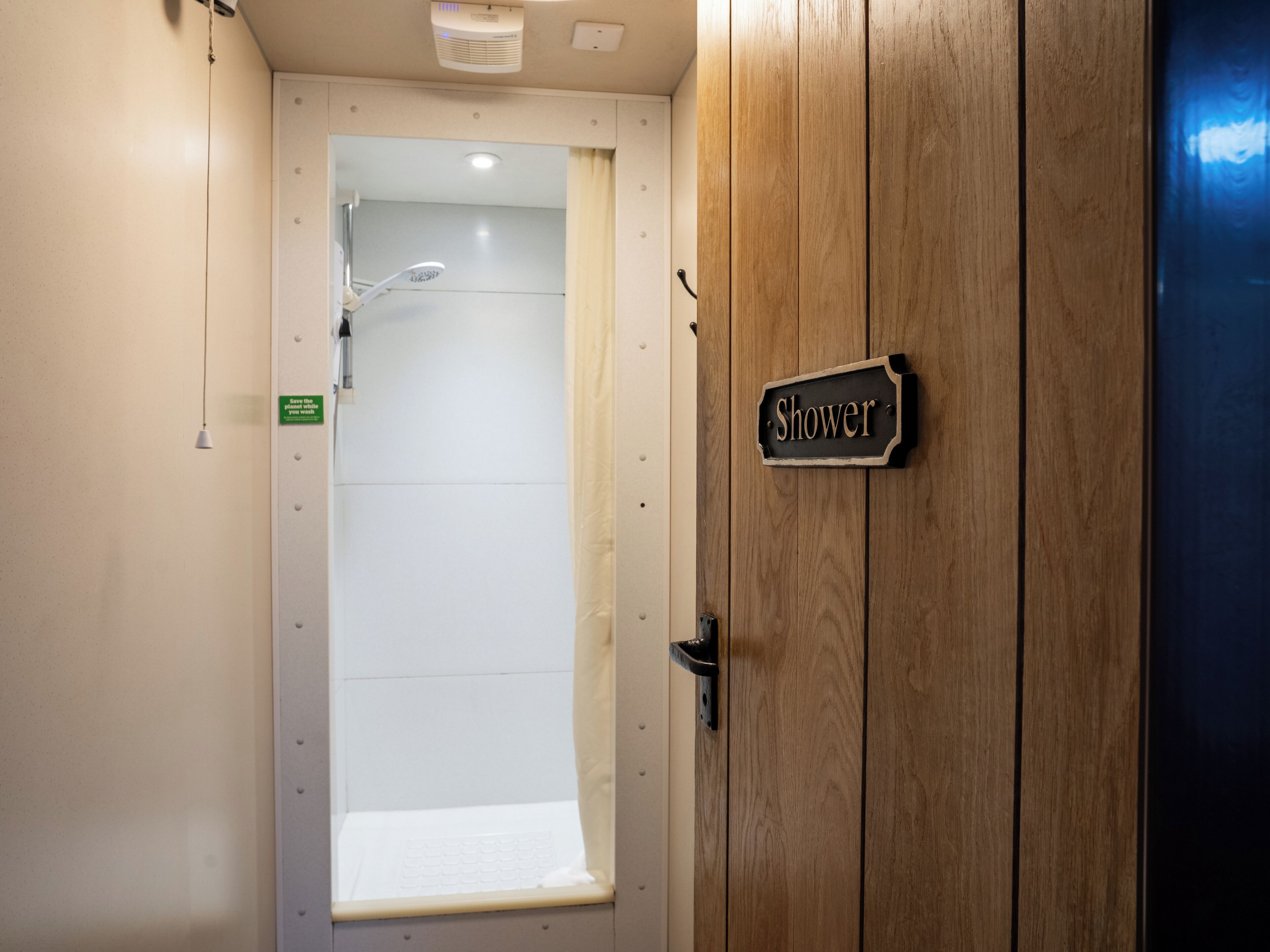 A wooden door with a "Shower" sign, a white tiled shower area, and a small window.