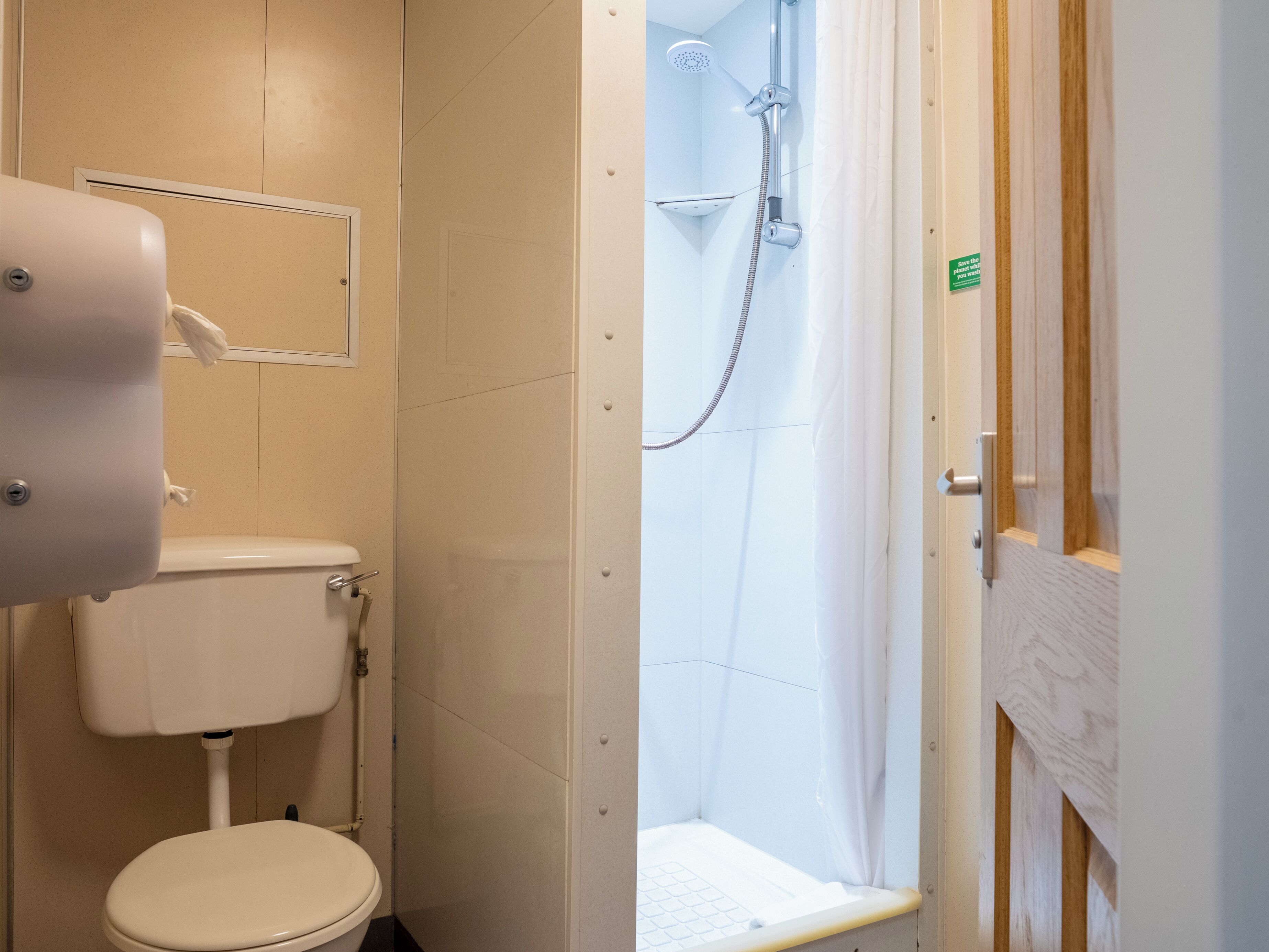 A small bathroom with a toilet, a shower, and a door.