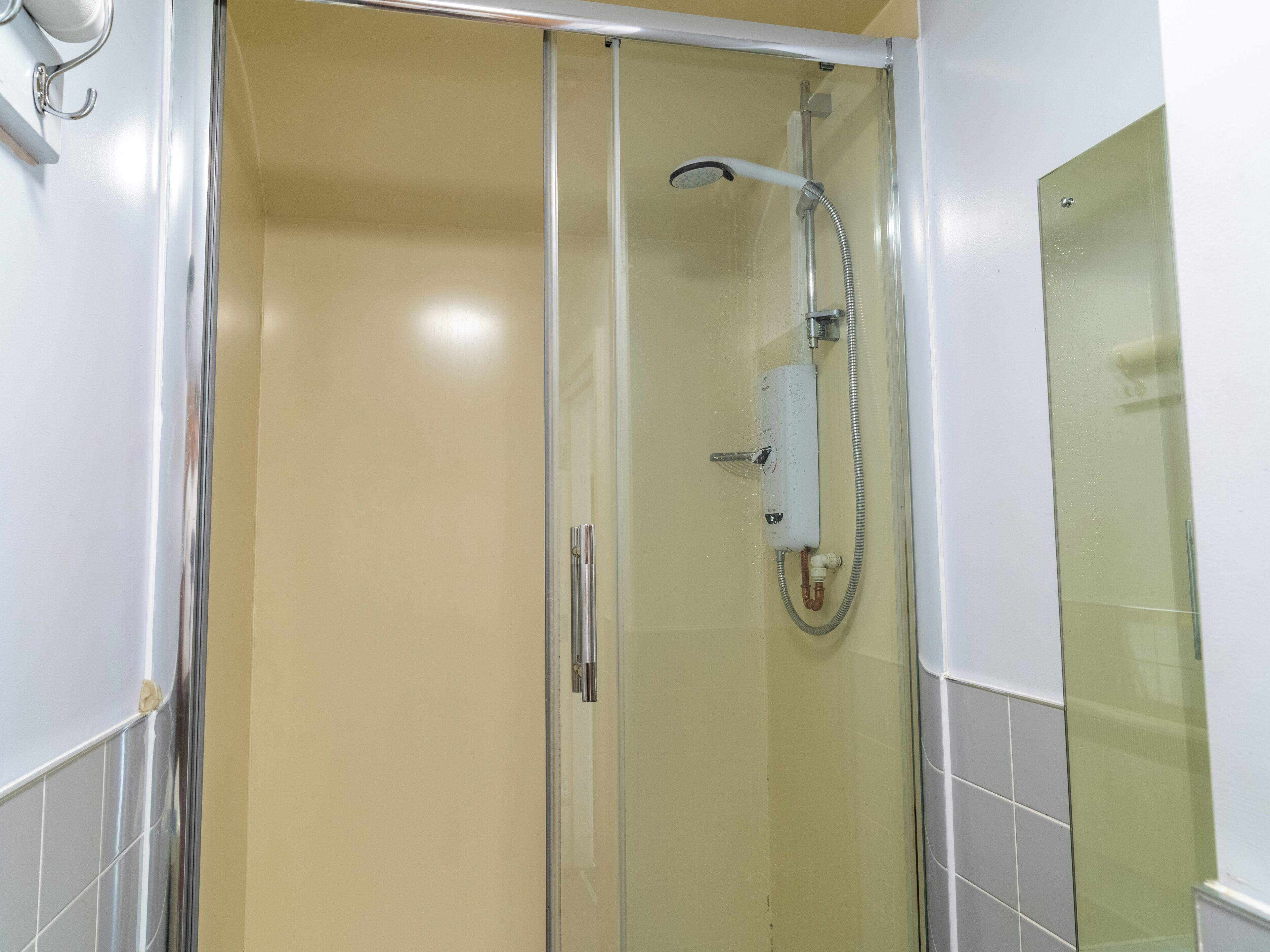 A glass-enclosed shower stall with a handheld showerhead and a wall-mounted control panel.