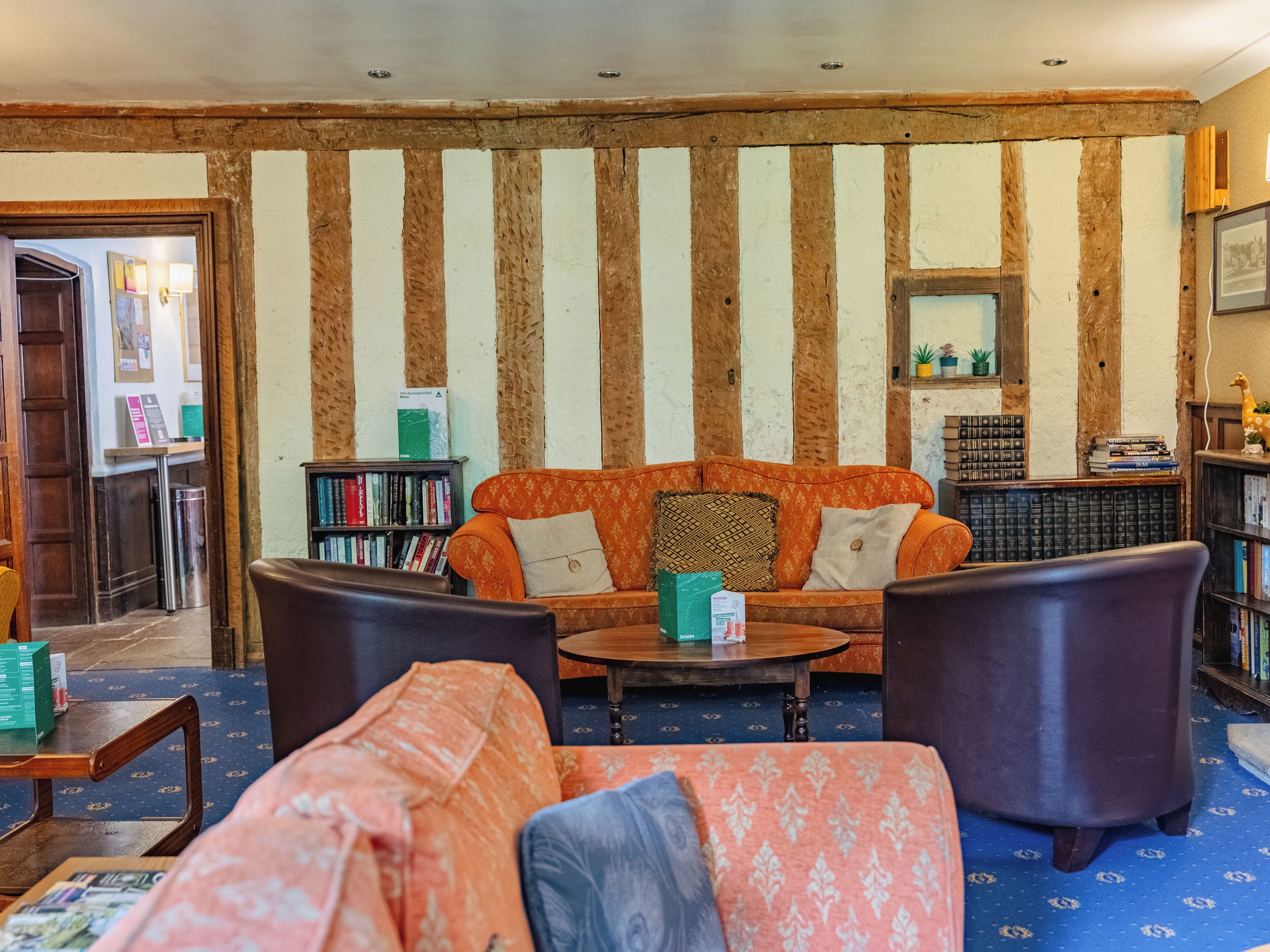 A cozy living room with striped wooden walls, a sofa, two armchairs, a coffee table, and a bookshelf.