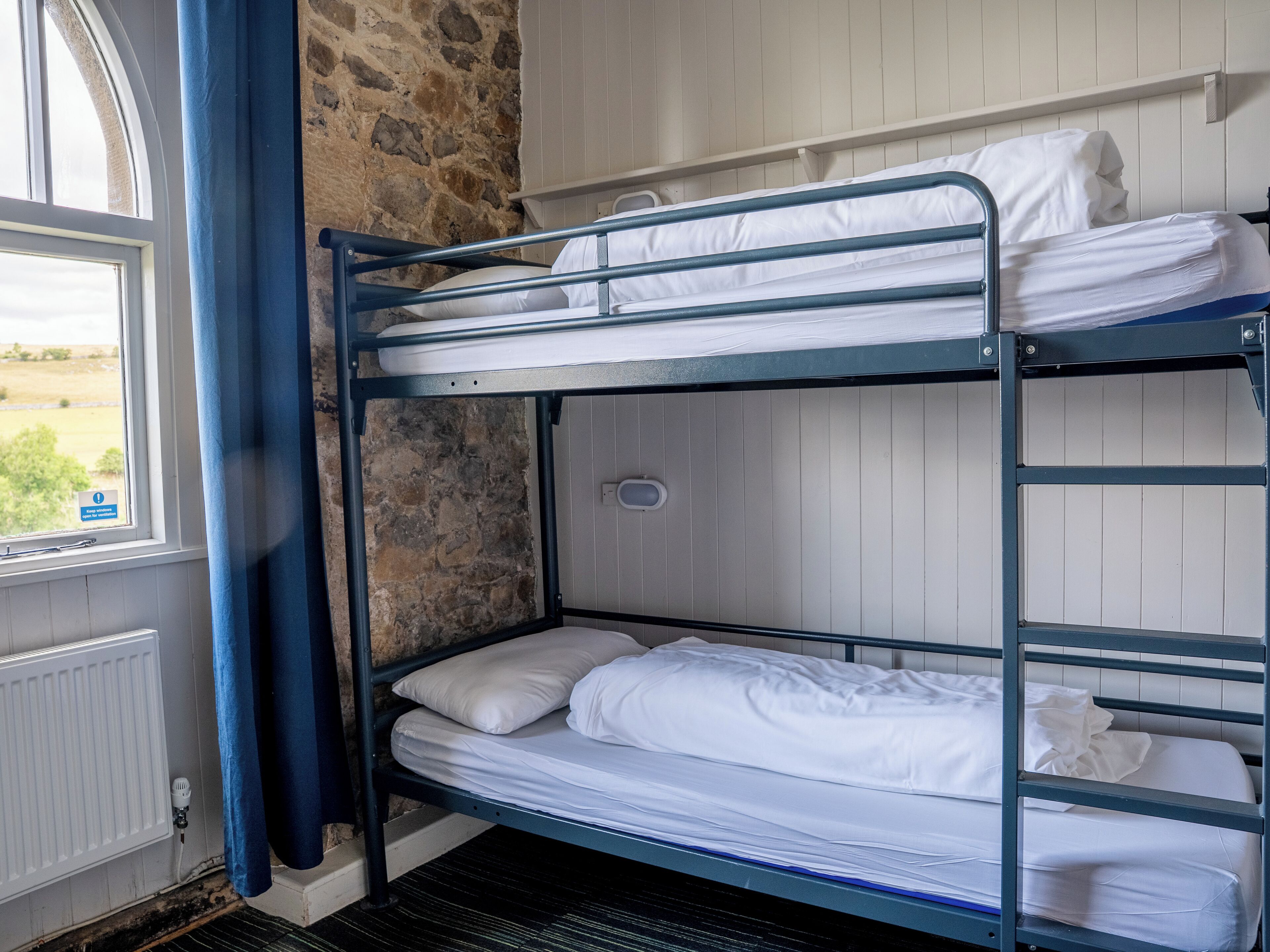 Une chambre avec un lit superposé, du linge de lit blanc et un mur en pierre.