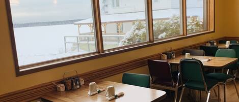 A dining area with wooden tables and chairs, large windows with a view of a snowy landscape, and pendant lighting.
