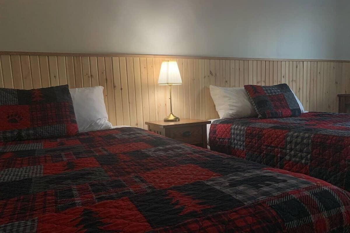 A room with two beds, a nightstand, and a lamp.