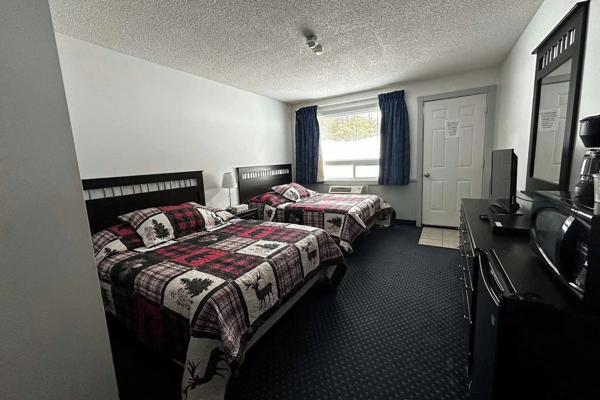A hotel room with two beds, a desk with a computer, a television, and a window with curtains.