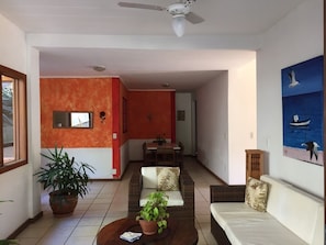 Una sala de estar con un sofá, una mesa de centro con plantas, una zona de comedor con una mesa y sillas, y un ventilador de techo.