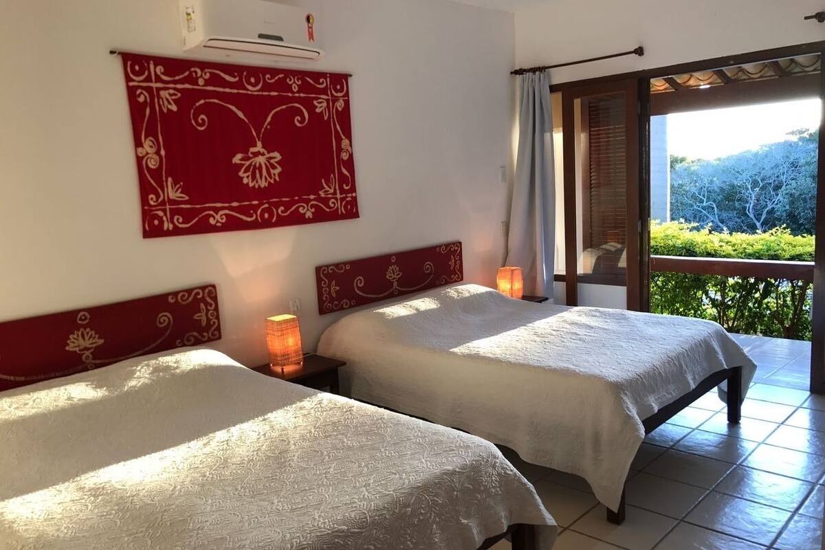 Habitación de hotel con dos camas, un tapiz decorativo rojo, un equipo de aire acondicionado y vistas a zonas verdes a través de una puerta de cristal.
