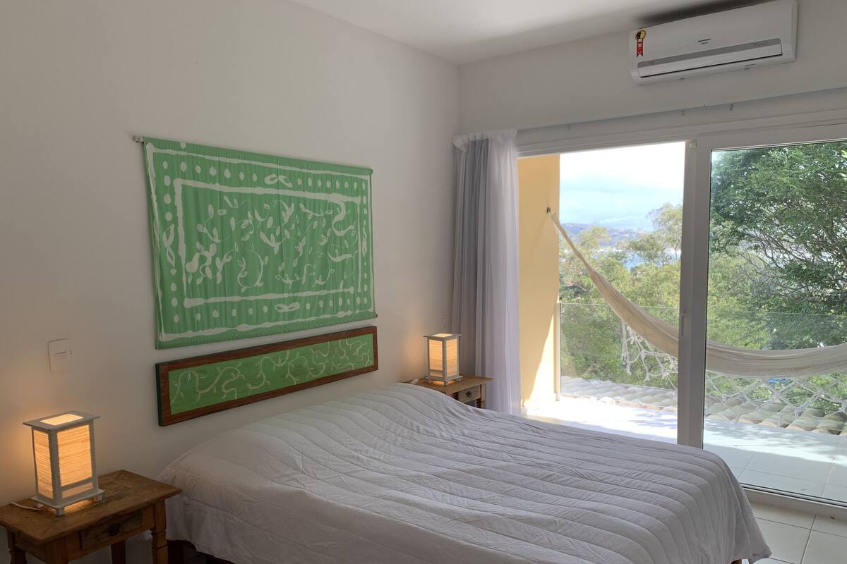 Un dormitorio con cama, un tapiz verde estampado, dos lámparas de noche y un ventanal con vistas a árboles y colinas.