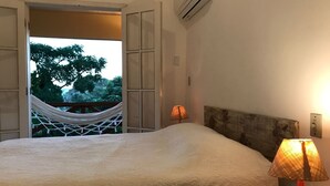 Un dormitorio con una cama grande, una hamaca fuera de la puerta y dos lámparas de noche.