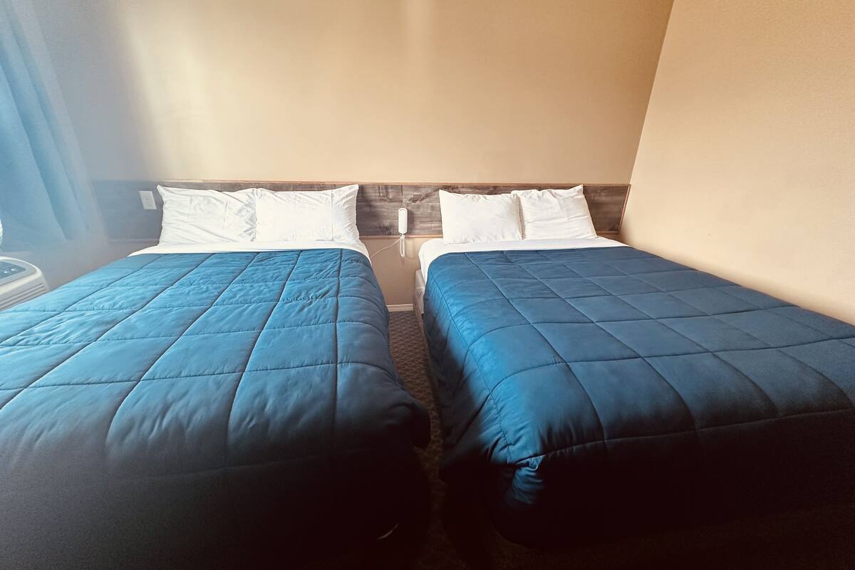 Zwei Einzelbetten mit blauer Bettwäsche, Holz-Kopfteile und weißen Kissen.