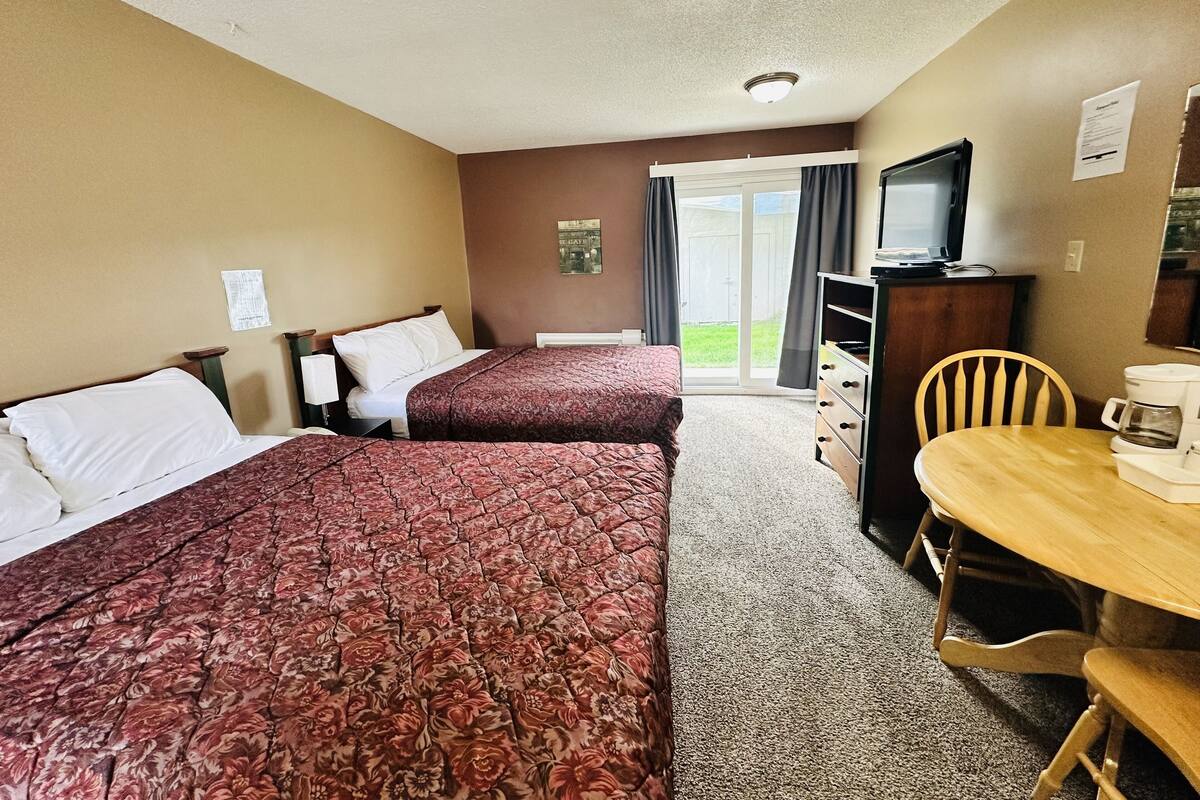Ein Hotelzimmer mit zwei Betten, einem Schreibtisch mit Stuhl, einem Fernseher und einer Kaffeemaschine.