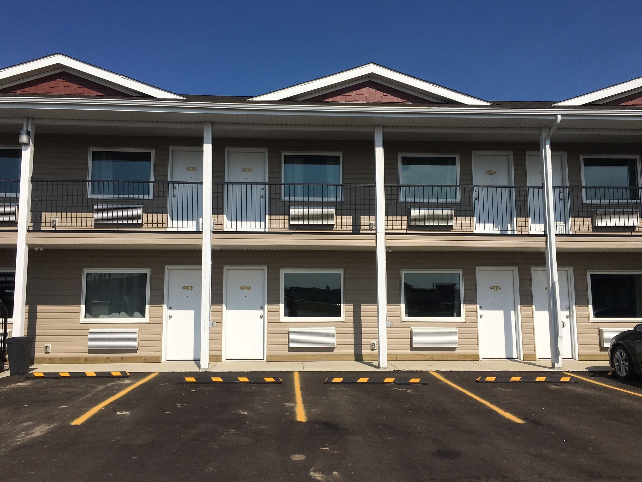 A multi-story motel with individual rooms on each floor, each with a door and window, and a parking lot in front.