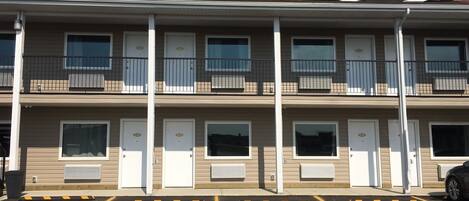 Un motel de varios pisos con habitaciones individuales en cada nivel, cada una con puerta y ventana, y un estacionamiento al frente.