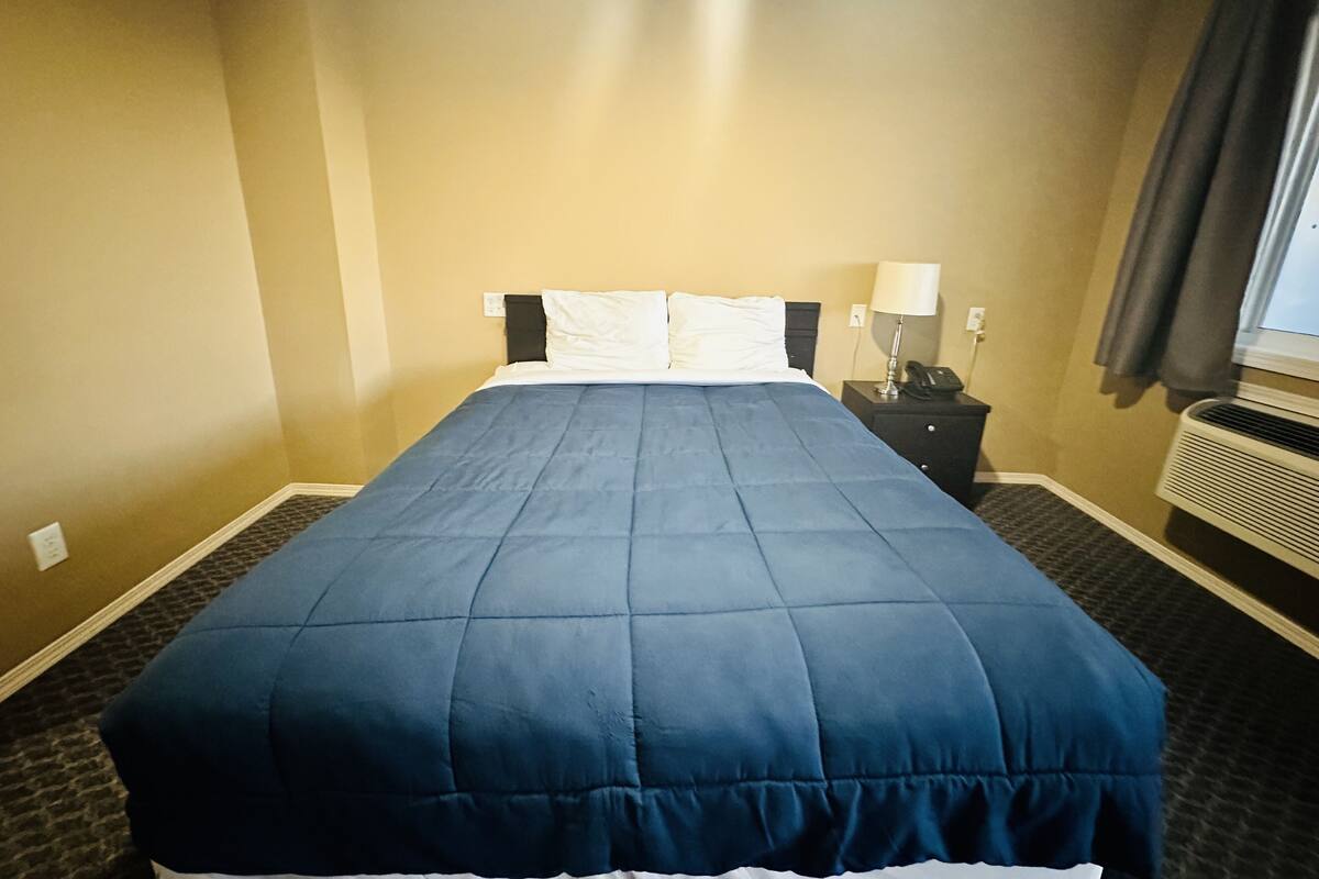 Ein Hotelzimmer mit einem großen Bett, einem Nachttisch mit Lampe und einer Klimaanlage.