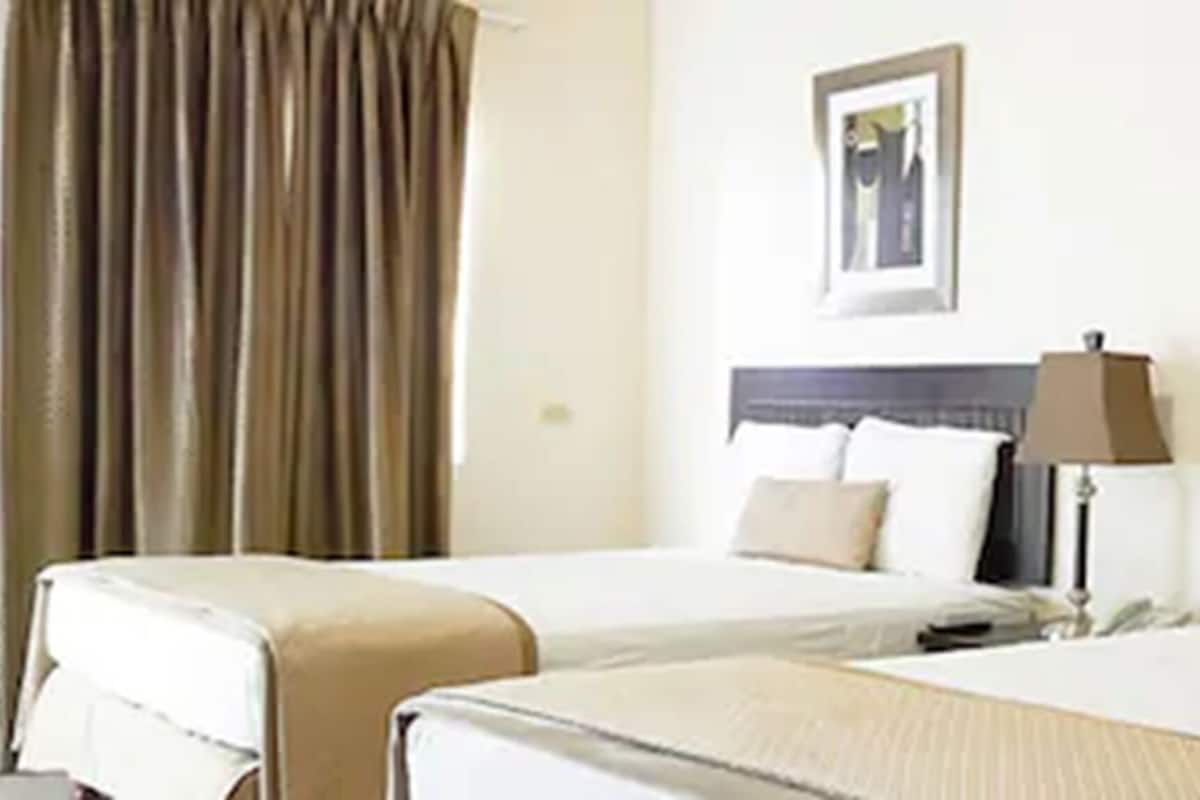 A hotel room with two beds, a nightstand, a lamp, and a framed picture on the wall.