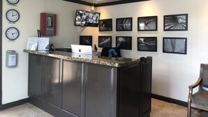 A reception area with a counter, clocks indicating different time zones, a television, and framed artwork on the walls. - Palms Hotel Trinidad (Arouca)